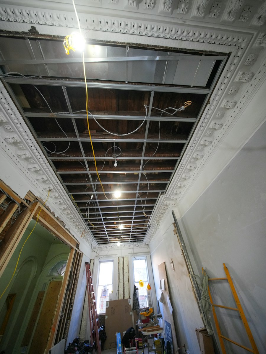 An Altbau hallway mid-renovation: the ceiling opened up to the old beams, new wiring hanging down, the original stucco cornice still in place